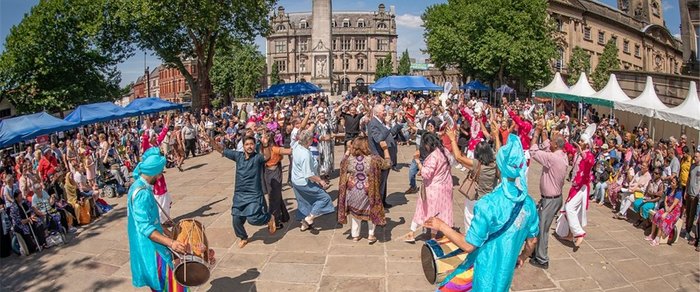 Performers in costume on a Preston street during the Mela, with a crowd behind them