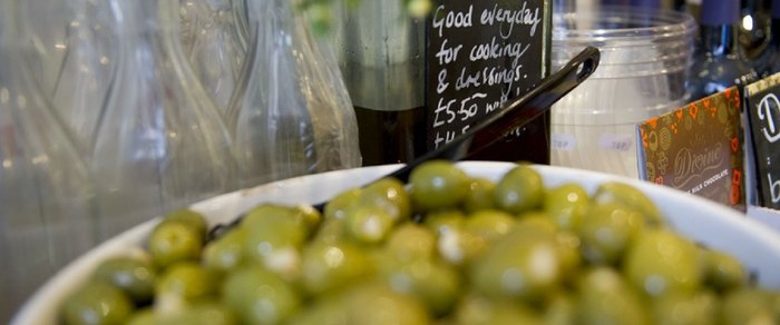 Olives and produce on a counter with a handwritten board behind