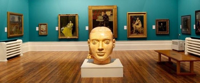 A gallery interior hung with paintings, a sculpted bust in the foreground