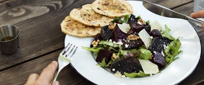 A plate of beetroot, walnut and rocket salad with flatbreads, on a wooden table beside a small jug of dressing