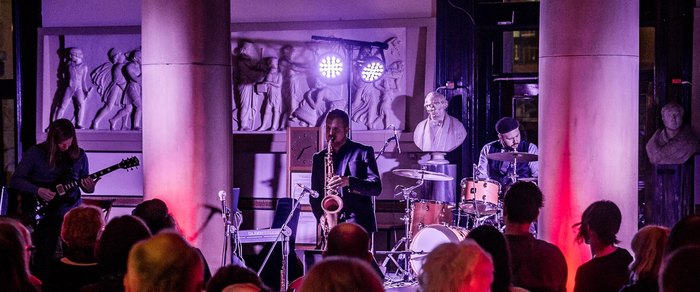 A band performing in a small live music room under coloured lighting