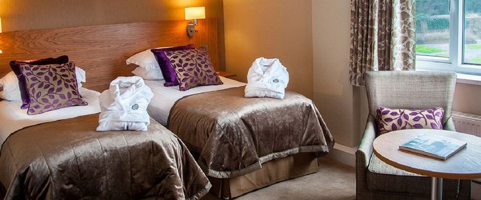 A twin hotel room with beds made and a table by the window